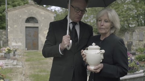 Mourners standing at funeral with cremation urn