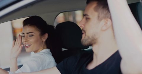 Cool couple having fun singing and dancing while driving car. Charming brunette woman and handsome man spending time together