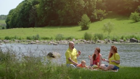 A family of four persons - father, mother, son and daughter, have a rest on the nature on the bank of the river