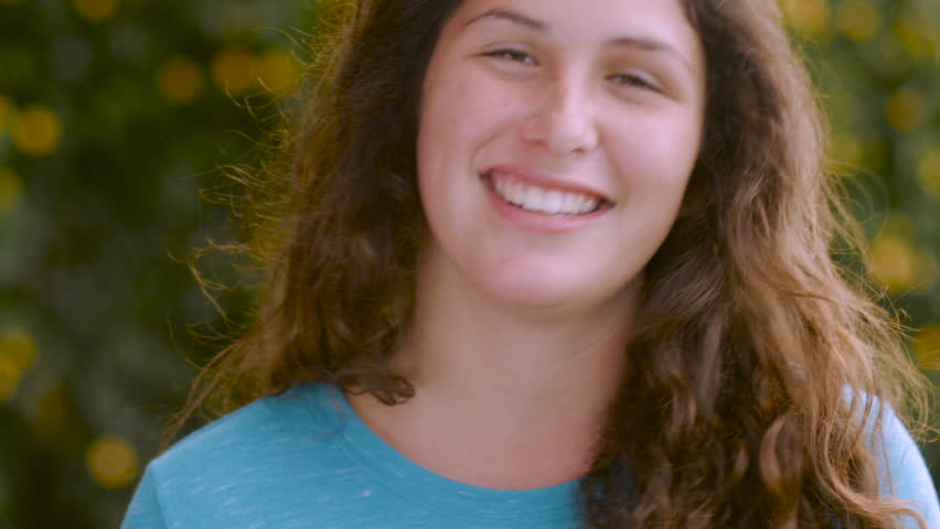 A beautiful young woman with long brown hair points with both hands at the camera and winks