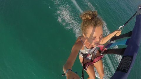 Young Female Tourist in Bikini Parasailing in Blue Sky over Sea