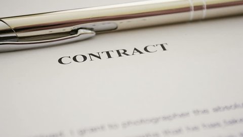 Contract abstract. Signing contract. "Contract" header on the sheet of paper, the person signs a document. Title "Contract" is printed in bold text. Texture of paper, closeup view.