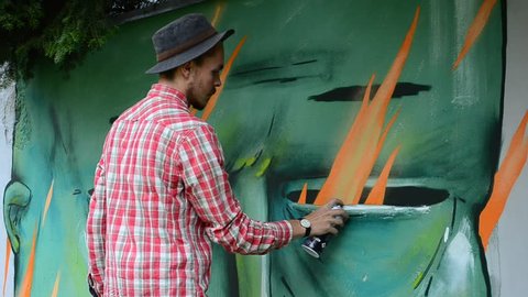 The artist draws graffiti on a fence.