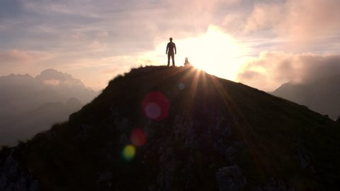 Aerial - Moving above silhouette of a man standing on top of the mountain. Man raising arms victoriously after climbing the mountain