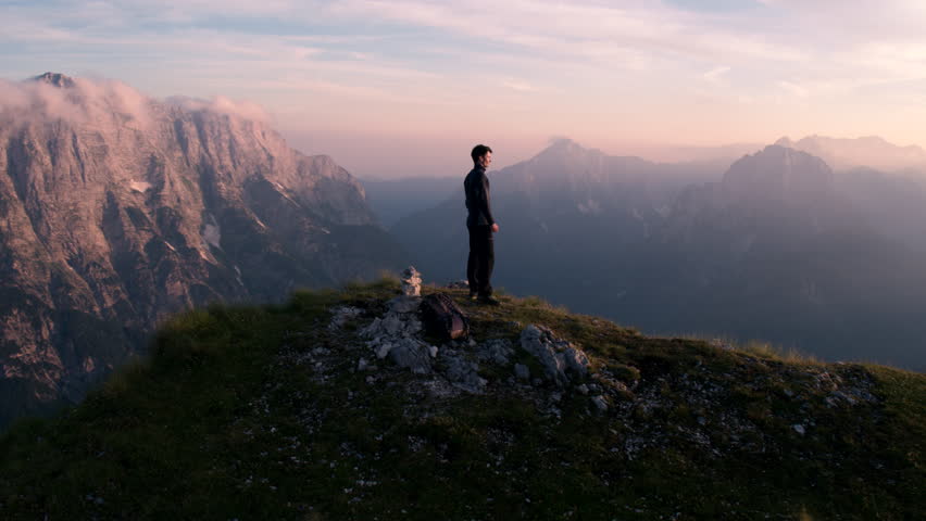 Aerial - Flying around young man standing victoriously on top of the mountain at sunset Royalty-Free Stock Footage #18395326