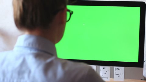 A freelancer working on a computer plastered with notes, reminders, stickers. On the monitor green screen, chroma key.
