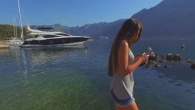 girl search in smartphone in picturesque bay with yacht and mountains view