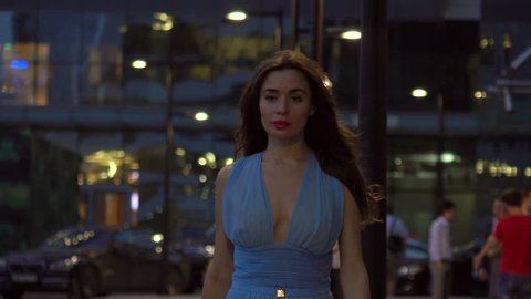 Beautiful brunette girl in blue dress walking on the street at night, 4K clip