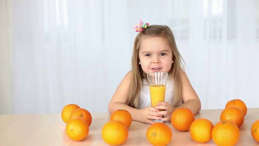 Llittle girl laughs at the camera. On the table lay oranges