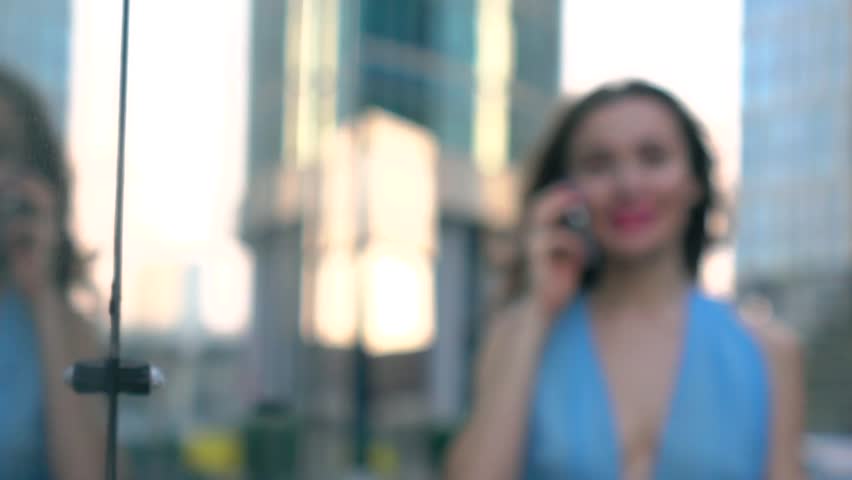 Cheerful brunette girl in blue dress talking on her phone on the street, super slow motion bokeh shot, 250 fps