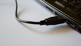 Plugged USB cable to laptop. Device plugged via USB connection, socket closeup, white background.