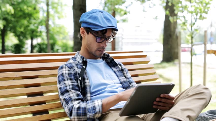 leisure, technology, communication and people concept - creative man with tablet pc computer sitting on city street bench over fixed gear bicycle