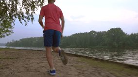 Steadicam video of athletic man running along sandy riverside, 4K