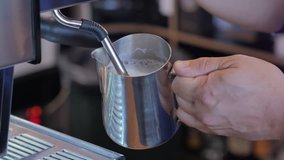 Barista steaming milk for cappuccino in coffee shop.