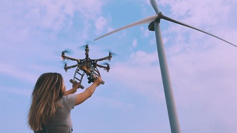 Drone takes off from the hands of a girl near a wind turbine, slow motion.
