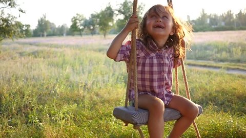Happy cute little child girl have fun sway spin on a swing on nature sunset