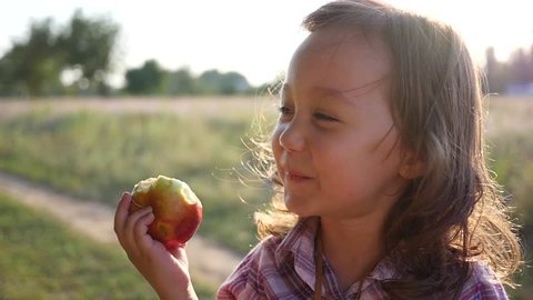 Cute little child girl portrait eating apple fruit on nature sunset light haze