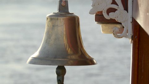 Closer look of the golden bell hanging on the side of the boat in the river