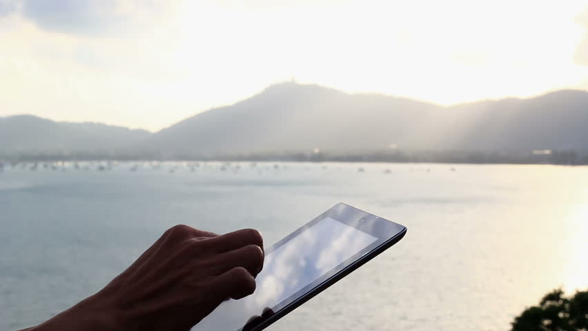 Close-up of man hands touching digital tablet in sunset background.