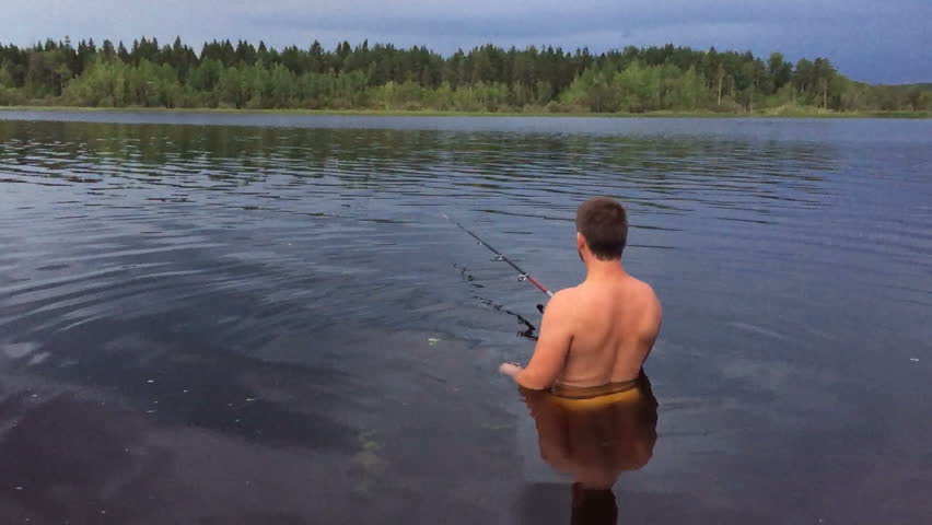 young man is fishing in the water up to his waist