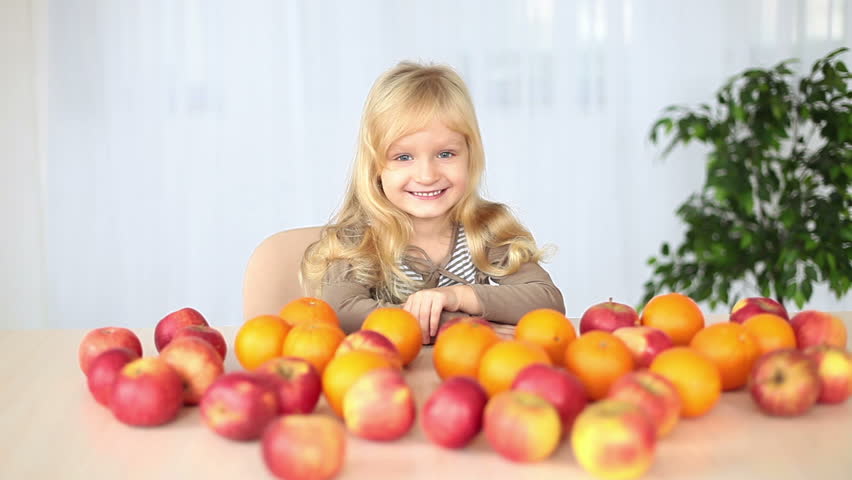 Laughing girl at the table. On the table lay oranges and apples