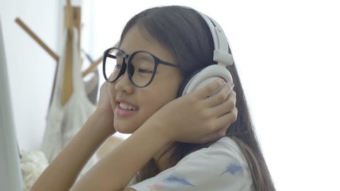 4K : Attractive Asian girl listening music on computer with headphone in the room, Pan shot