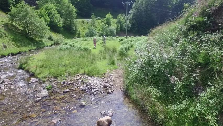 Couple crossing river stream in mountains with bikes