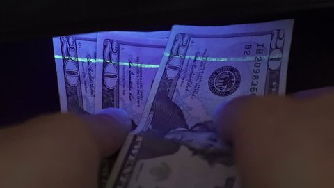 Closeup shot of an anonymous person putting USA currency under a black light to check for counterfeit or fake money.