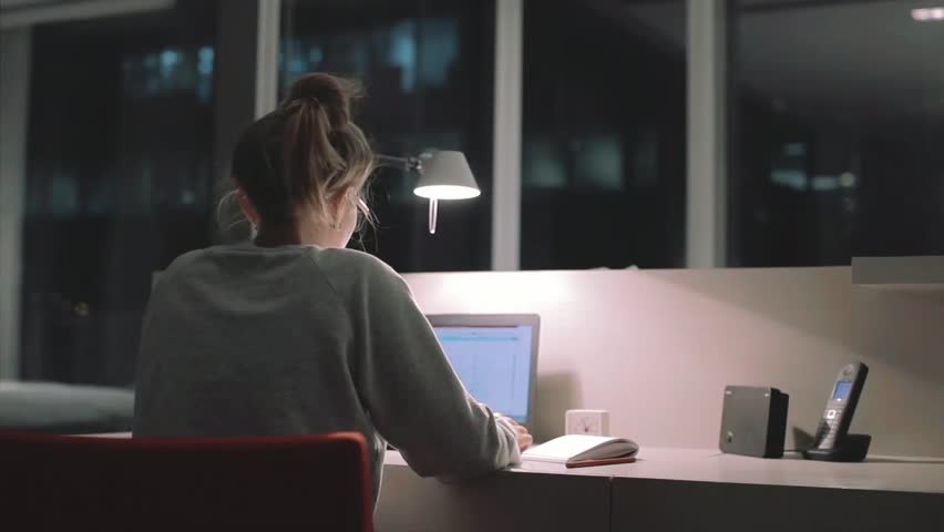 Young concentrated woman, sitting in her room or office with french windows in the dark at the lamp.Studies late at night.Staying up late. Woman feeling headache and pain in the neck.    | Shutterstock HD Video #18499021