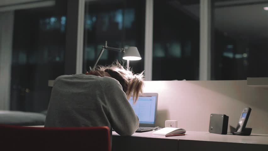 Young concentrated woman, sitting in her room or office with french windows in the dark at the lamp.Studies late at night.Staying up late. Woman feeling headache and pain in the neck.   