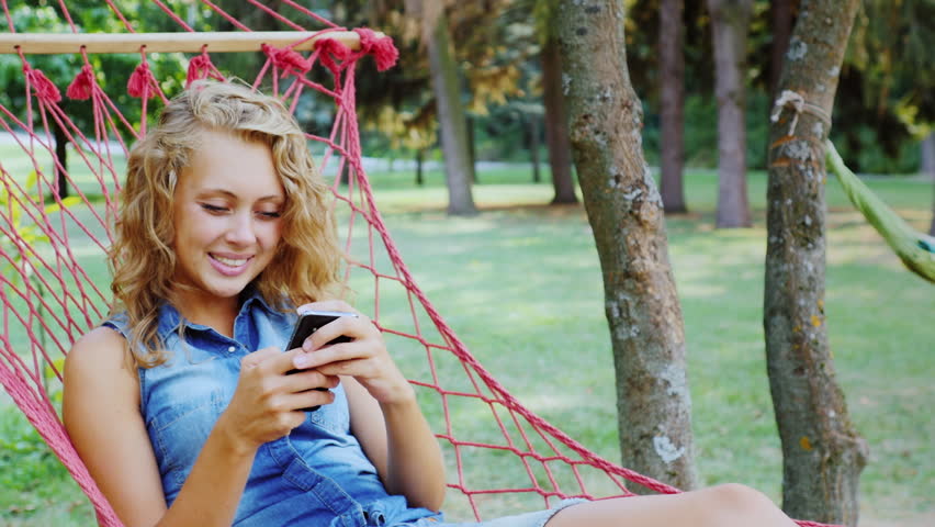 Attractive woman lying in a hammock, typing on smartphone