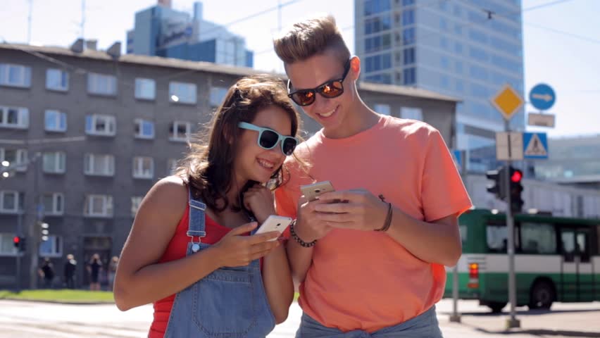 summer vacation, technology, augmented reality and people concept - happy teenage couple with smartphones playing game or shooting video in city