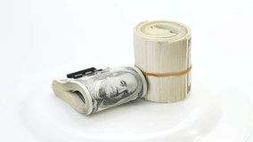 Bundle of many 100 dollar bank notes rolled up and fasten with paper clip rotating on a white background