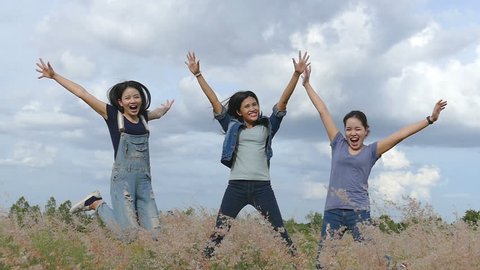 Three friends, young asian girls enjoy nature jumping in fields , slow motion. 