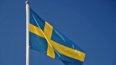 A Swedish flag flutters in the wind against a blue sky background