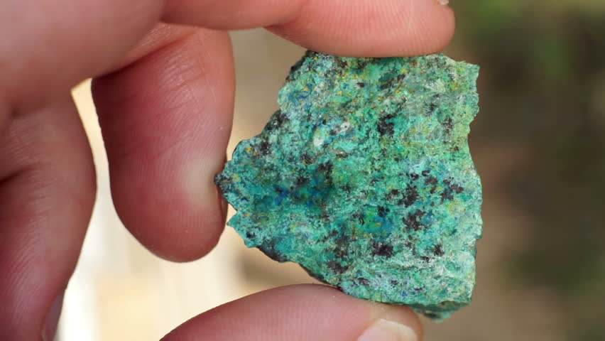 Close up shot of the hand of an anonymous prospector or geologist holding a rock chip sample of copper oxide ore used in the mining industry to extract copper base metal to sell as a commodity.