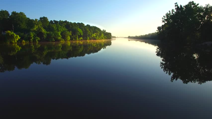 Sunrise escapes from the shadows over tranquil river surface.
