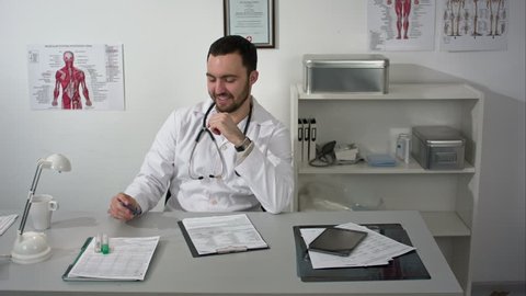Friendly male doctor looking to camera nods and smiling