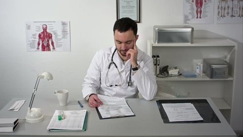 Young serious doctor sitting in medical office with folder and reading documents
