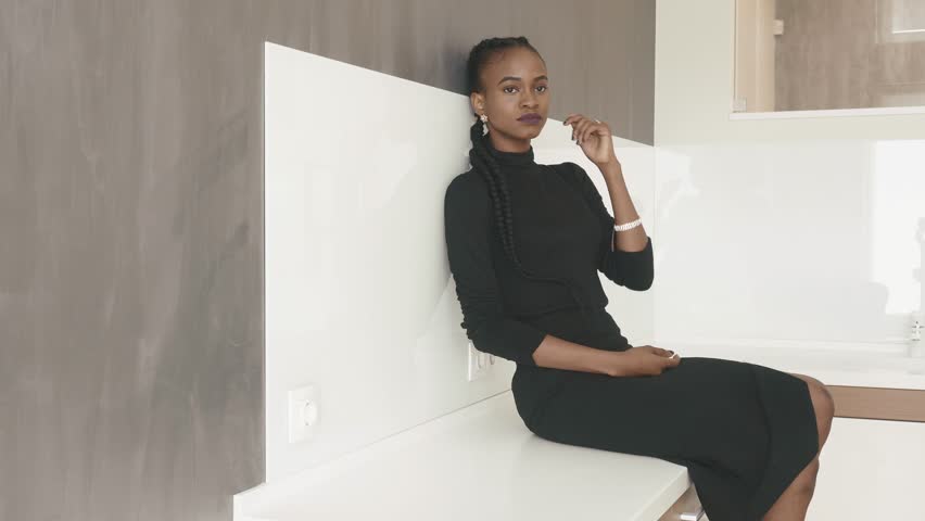 Serious African-American woman dressed in black sitting on the table leaned against the wall