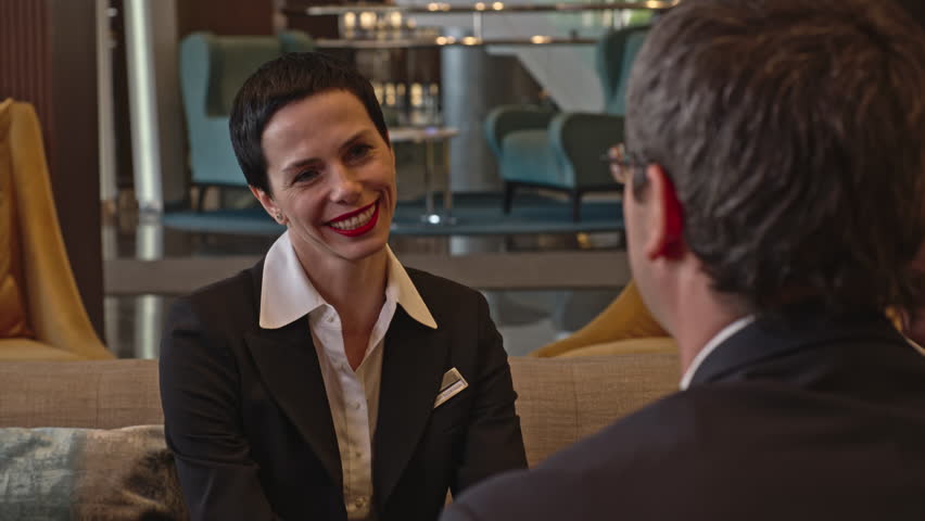 Attractive mid-adult businesswoman sitting on sofa in the hotel lobby and talking to her colleagues