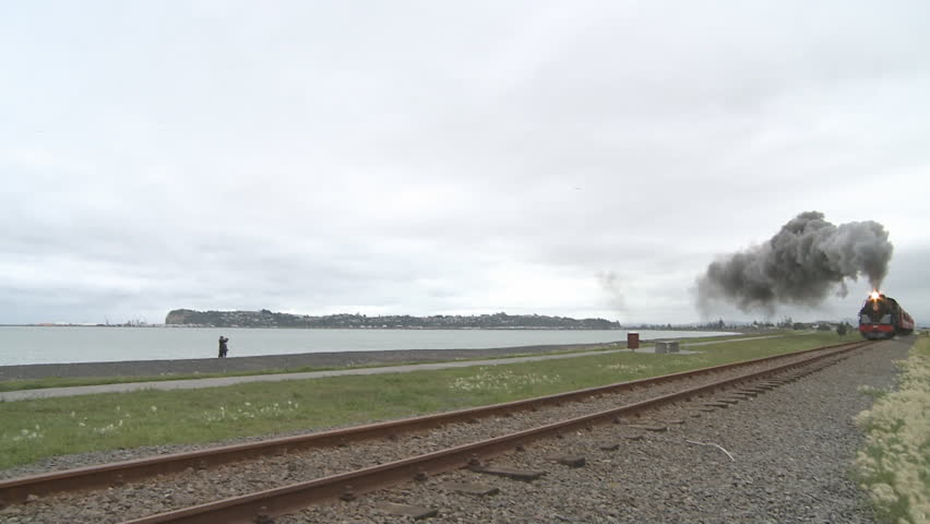 A vintage steam train and carriages on a holiday excursion pass by the coast. 