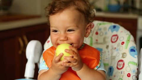 Baby is eating an apple in the kitchen
