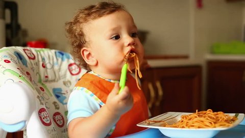 Baby is eating spaghetti with a fork
