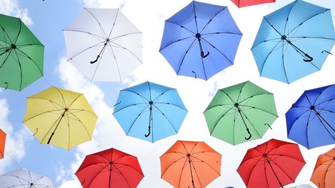 Multicolored umbrellas hanging over head on the street against the blue sky and swinging in the wind