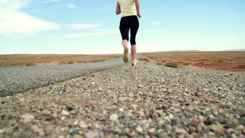 Young woman jogging on desert road, dolly shot, slow motion 