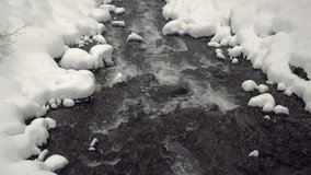 Heavy snow falls over a snow lined river. Shot with a high speed camera for a slow motion effect.