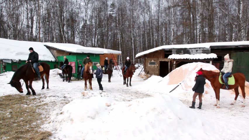 Several people sit horseback on stable yard at winter day