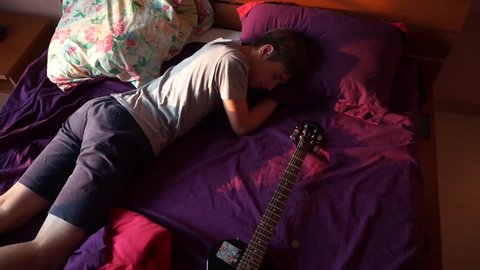 boy lying on the bed. boy and his guitar. every morning he wakes up with a guitar. Good morning and cheerful Guitar. boy lying in bed in the morning
