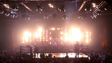 Lot of people in large hall on fighting event, girls dance on stage with bright illumination